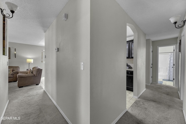 hall with light carpet, arched walkways, a textured ceiling, and baseboards