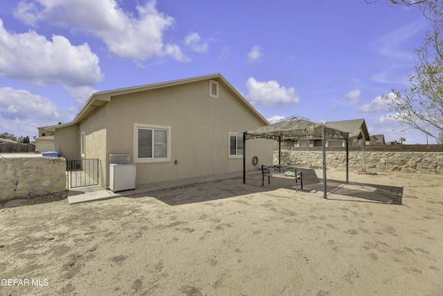 back of property with a gate, fence, stucco siding, a gazebo, and a patio area