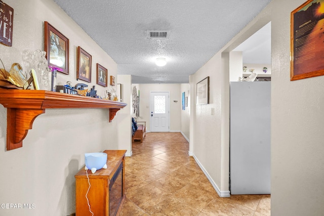 hall featuring light tile patterned floors, visible vents, a textured ceiling, and baseboards