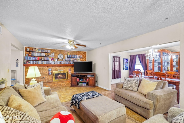 living area with ceiling fan with notable chandelier, a brick fireplace, and a textured ceiling