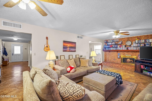 living room with a ceiling fan, visible vents, a fireplace, a textured ceiling, and tile patterned floors