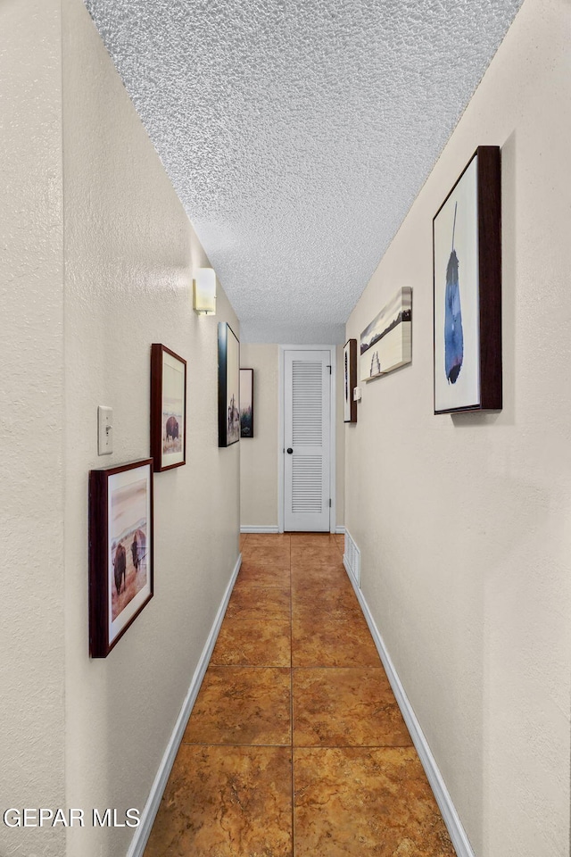 hallway featuring baseboards, visible vents, and a textured ceiling