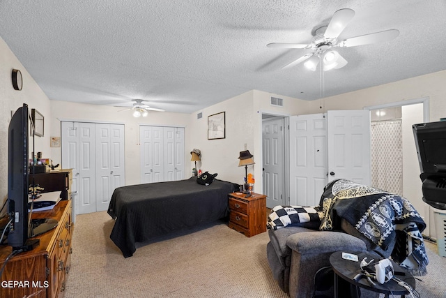 bedroom with two closets, visible vents, light colored carpet, and a textured ceiling