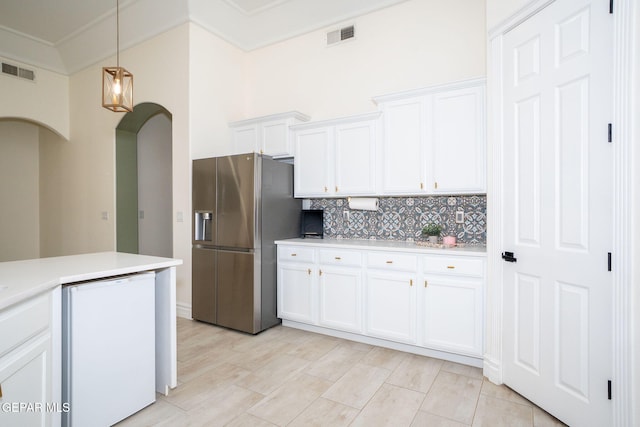 kitchen featuring visible vents, white cabinetry, stainless steel fridge, arched walkways, and light countertops