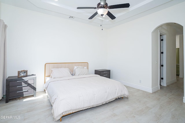 bedroom featuring visible vents, baseboards, a tray ceiling, arched walkways, and ceiling fan