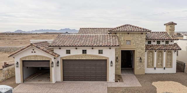 mediterranean / spanish-style house with a tiled roof, decorative driveway, an attached garage, and stucco siding