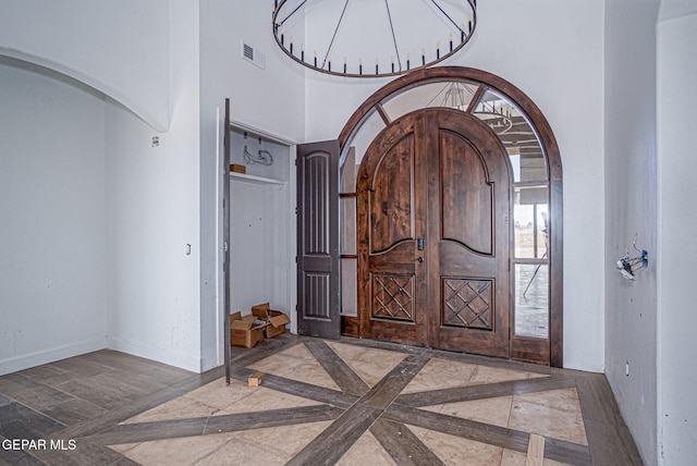 foyer featuring visible vents, marble finish floor, arched walkways, a high ceiling, and baseboards