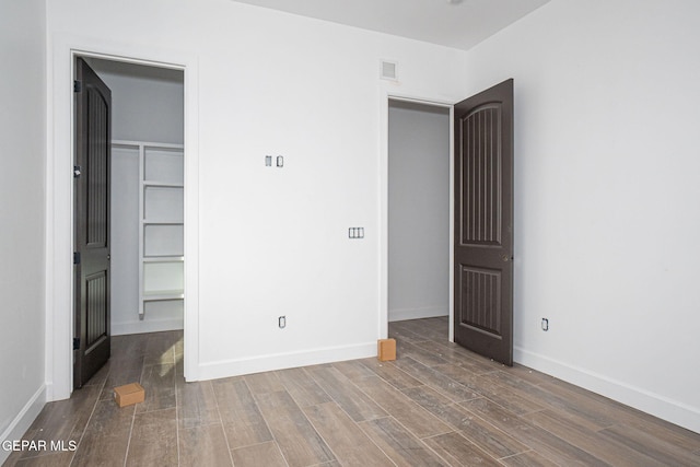 unfurnished bedroom with visible vents, baseboards, wood finished floors, and a spacious closet