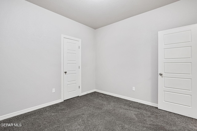 spare room featuring baseboards and dark colored carpet