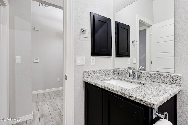 bathroom featuring baseboards, vanity, wood tiled floor, and a textured wall