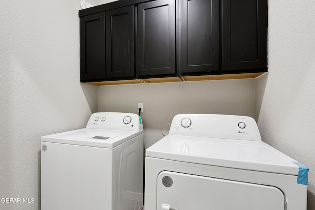 clothes washing area featuring cabinet space, washer and dryer, and a textured wall