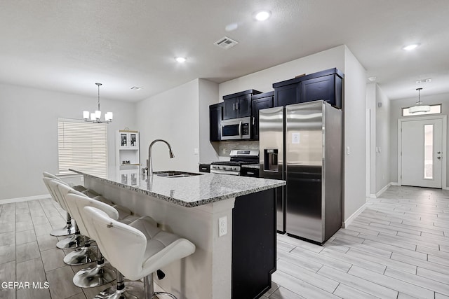 kitchen with visible vents, a breakfast bar, a sink, appliances with stainless steel finishes, and light stone countertops