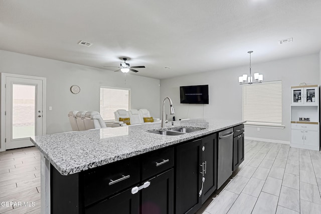 kitchen with a center island with sink, visible vents, a sink, ceiling fan with notable chandelier, and dark cabinets