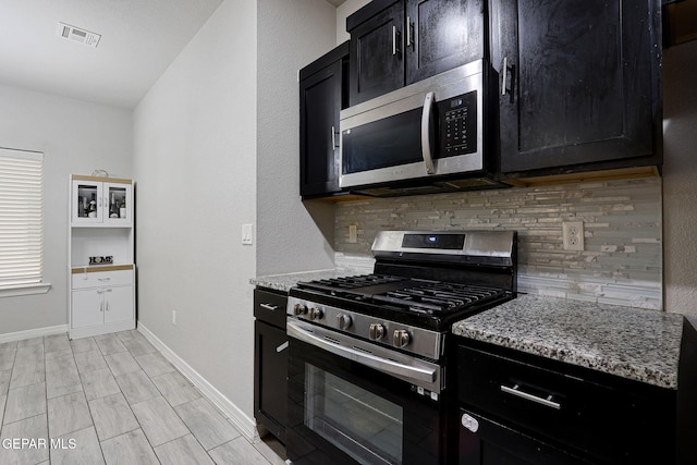 kitchen featuring visible vents, backsplash, light stone countertops, stainless steel appliances, and dark cabinets