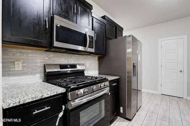 kitchen with backsplash, dark cabinetry, appliances with stainless steel finishes, baseboards, and light stone countertops