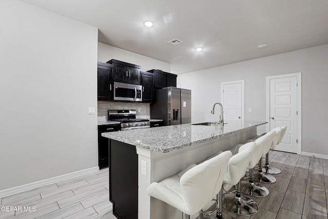 kitchen with dark cabinetry, visible vents, a sink, appliances with stainless steel finishes, and tasteful backsplash