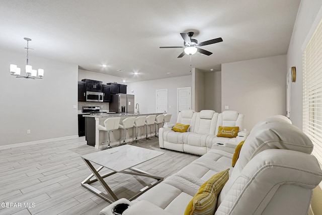 living area with light wood-style flooring, ceiling fan with notable chandelier, and baseboards