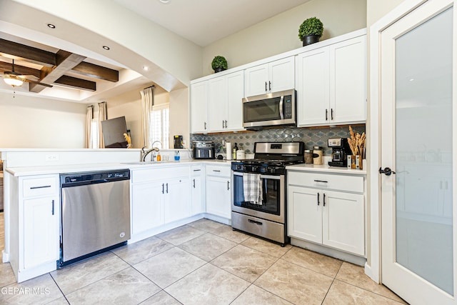 kitchen with coffered ceiling, a sink, stainless steel appliances, light countertops, and tasteful backsplash