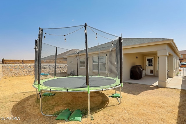 rear view of house featuring a patio, a trampoline, fence, and stucco siding