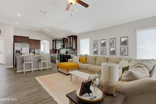 living room with a wealth of natural light, visible vents, vaulted ceiling, and wood finished floors