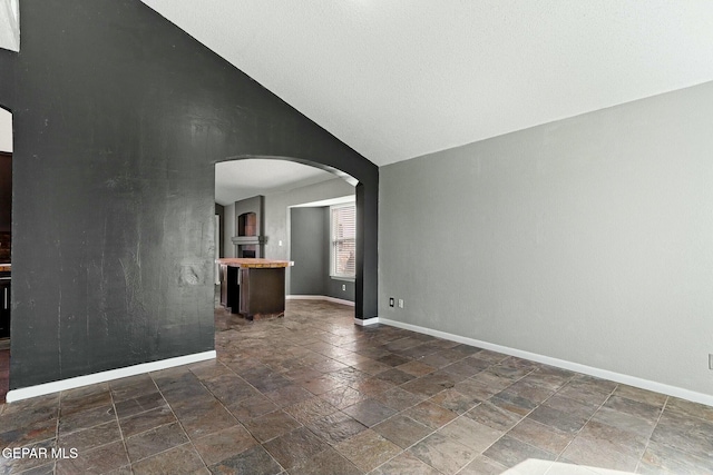 empty room featuring arched walkways, stone finish floor, high vaulted ceiling, and baseboards