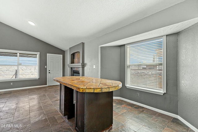 kitchen with vaulted ceiling, a fireplace, baseboards, and stone tile flooring