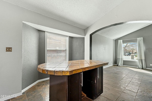 kitchen with lofted ceiling, tile countertops, baseboards, and stone tile floors