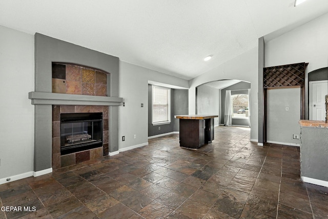 unfurnished living room with lofted ceiling, stone tile floors, arched walkways, a fireplace, and baseboards