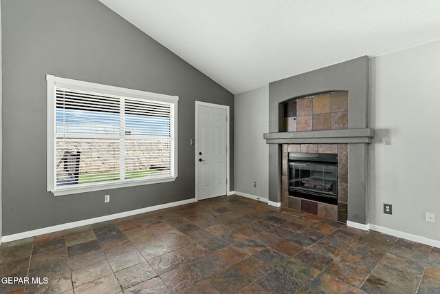 unfurnished living room featuring a fireplace, stone finish flooring, baseboards, and vaulted ceiling