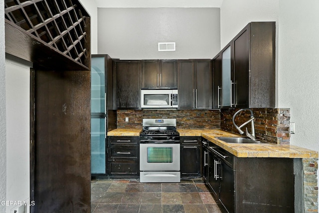 kitchen featuring visible vents, a sink, decorative backsplash, stainless steel appliances, and stone finish flooring