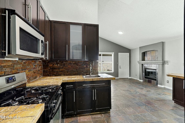 kitchen featuring a sink, stainless steel appliances, glass insert cabinets, baseboards, and a tile fireplace