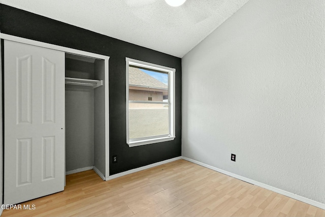 unfurnished bedroom with baseboards, light wood-style flooring, a textured wall, a closet, and a textured ceiling