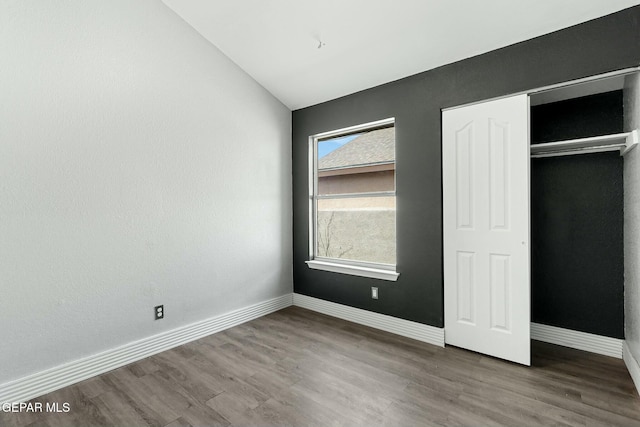 unfurnished bedroom featuring a closet, baseboards, wood finished floors, and vaulted ceiling