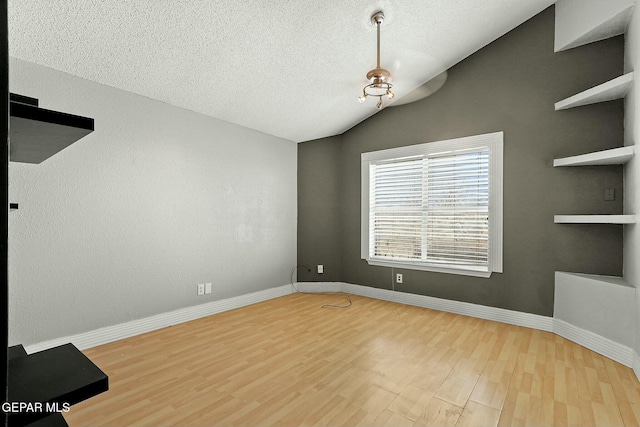 unfurnished room with lofted ceiling, wood finished floors, baseboards, and a textured ceiling