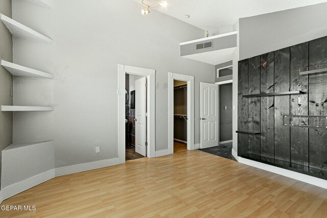 unfurnished bedroom with a spacious closet, wood finished floors, visible vents, and baseboards