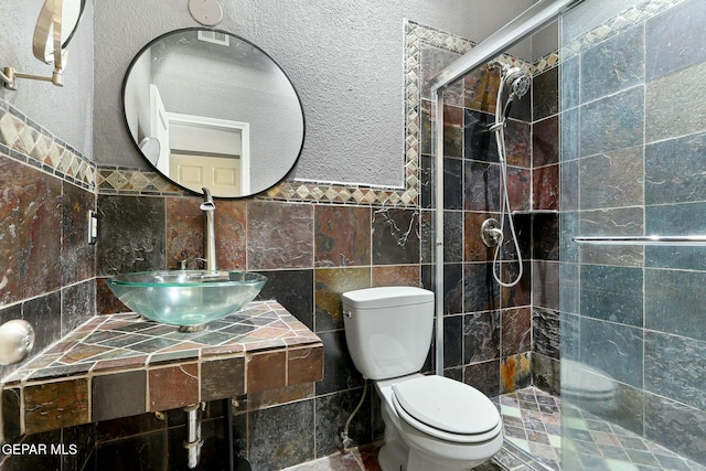 full bath with toilet, a sink, tile walls, tiled shower, and a textured wall