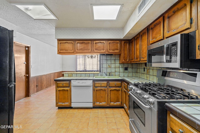 kitchen with wainscoting, appliances with stainless steel finishes, and tile counters