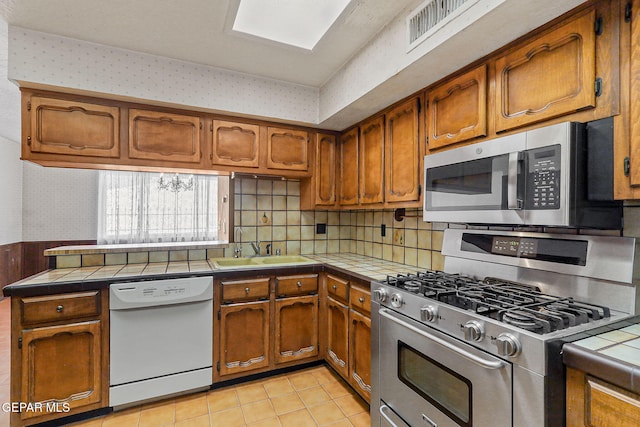 kitchen featuring a sink, appliances with stainless steel finishes, tile counters, and wallpapered walls