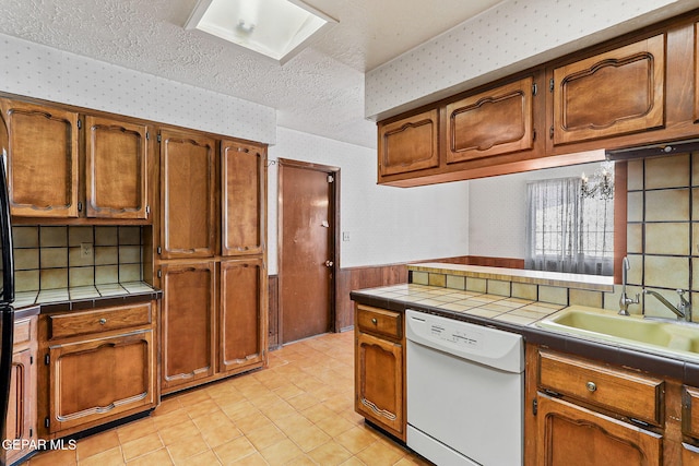 kitchen featuring a sink, tile counters, white dishwasher, and wallpapered walls