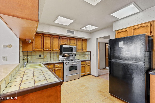 kitchen featuring visible vents, a sink, backsplash, tile countertops, and stainless steel appliances