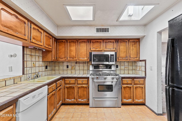 kitchen featuring tile countertops, stainless steel appliances, brown cabinets, and visible vents