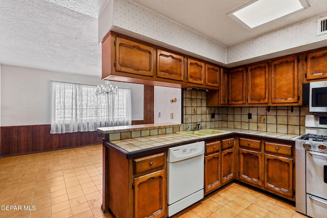 kitchen with wallpapered walls, tile counters, wainscoting, stainless steel appliances, and a textured ceiling