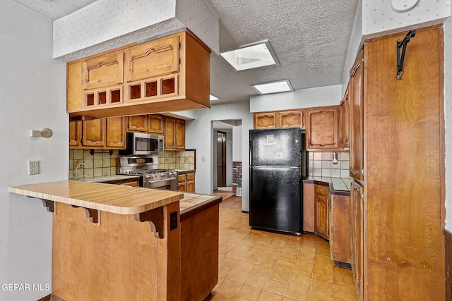 kitchen featuring brown cabinets, appliances with stainless steel finishes, a breakfast bar area, and a peninsula