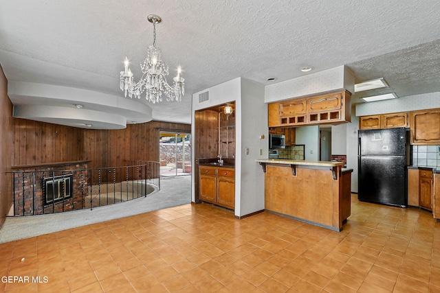 kitchen with visible vents, a peninsula, freestanding refrigerator, stainless steel microwave, and a brick fireplace