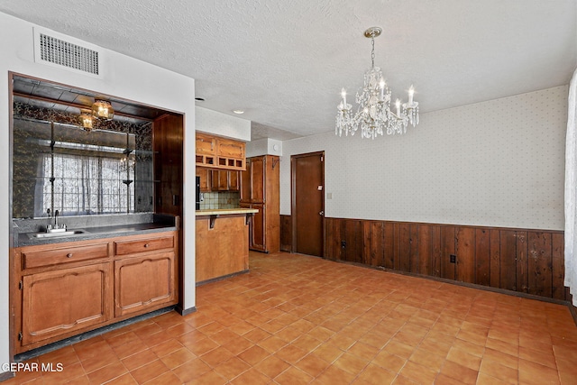 kitchen with a wainscoted wall, a textured ceiling, wallpapered walls, and visible vents