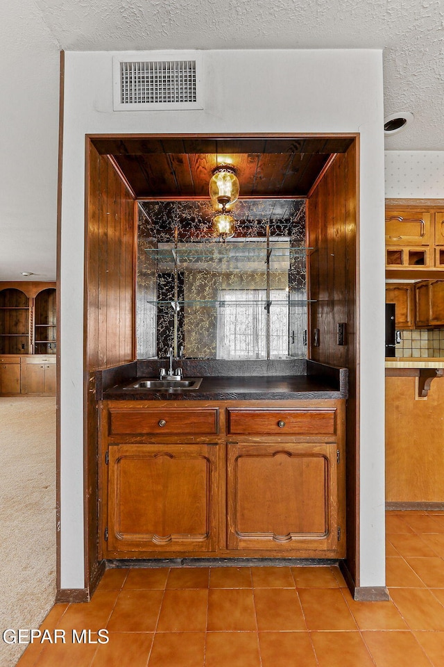 bar with a sink, visible vents, a textured ceiling, and light tile patterned floors