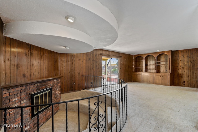 corridor featuring built in shelves, light carpet, an upstairs landing, and wood walls