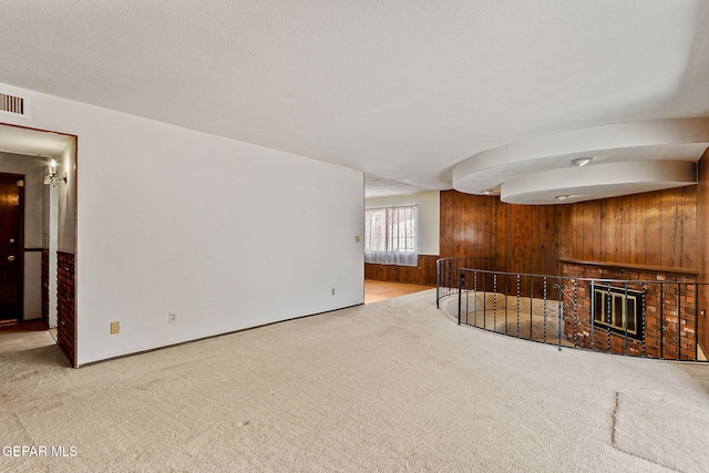 unfurnished living room featuring carpet, wood walls, a fireplace, and a textured ceiling