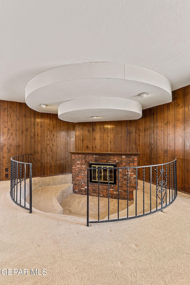 interior space with carpet flooring, wood walls, a brick fireplace, and a textured ceiling