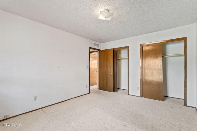 unfurnished bedroom featuring visible vents, a textured ceiling, multiple closets, and carpet floors